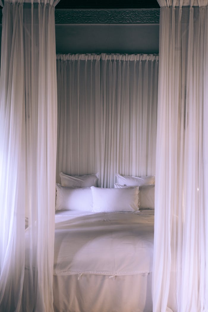 services-02 A cozy and serene canopy bed draped with translucent white curtains creating a tranquil bedroom setting.